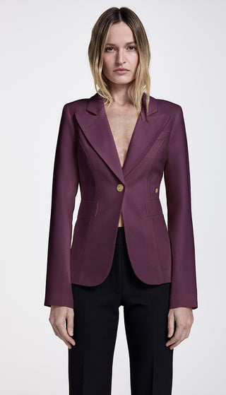 A woman wearing a purple single-breasted blazer with a peak lapel, brass buttons, and a cut-out back vent.