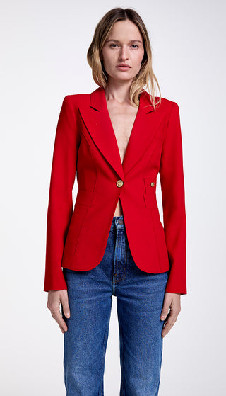 A woman wearing a red single-breasted blazer with a cut-out back vent and brass hardware, paired with blue jeans.