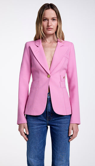 A model wearing a pink single-breasted blazer with a cut-out back vent and brass hardware, paired with blue jeans.