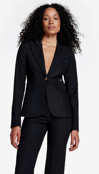 A woman wearing a black blazer with a double back vent and signature brass buttons, paired with matching trousers.