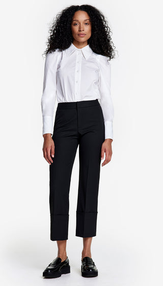 A model wearing a crisp, black, cuffed stretch pant with a straight cropped leg. The pant features wide cuffed hems and is paired with a white shirt.