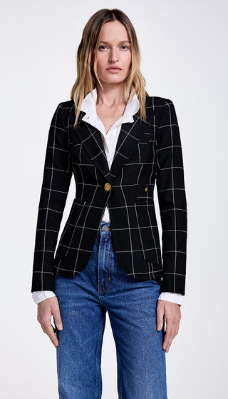 A woman wearing a black windowpane checkered blazer with mahogany elbow patches and brass buttons, paired with a white shirt and blue jeans.