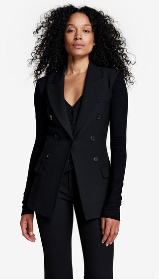 A woman wearing a double-breasted black blazer with jersey sleeves and a V-neck, paired with a black top and trousers.