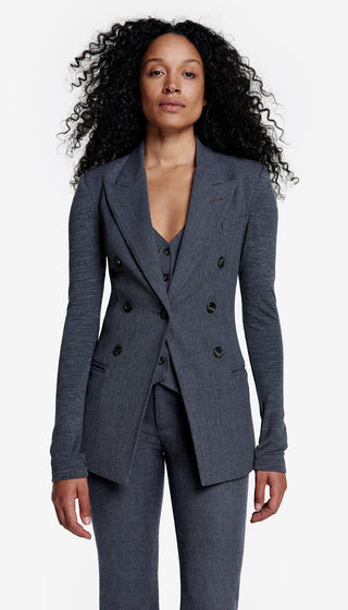 A woman wearing a charcoal gray double-breasted blazer with a peak lapel and jersey sleeves, paired with a coordinating waistcoat and pant.