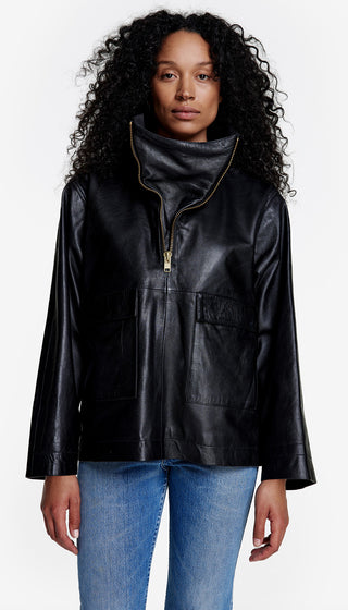 A model wearing a black over-the-head leather anorak with a funnel neck and brass zippers.