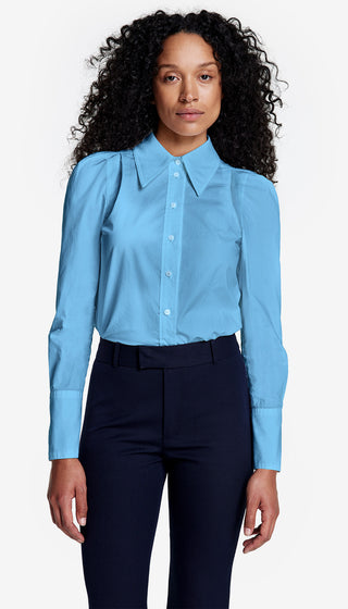A woman wearing a blue long-sleeved button-down shirt with a point collar and box pleat details.