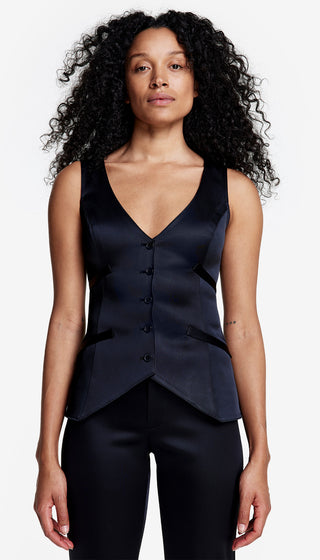 A woman wearing a black tuxedo waistcoat with a V-neckline, sleeveless design, and front button closure, paired with black trousers.