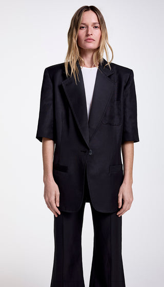 A model wearing a black short sleeve oversized blazer with wide notched lapel, paired with a white top and trousers.
