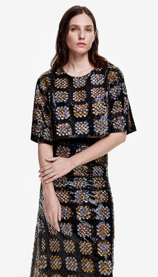 A woman modeling a black and gold sequin tee with a geometric pattern. The shirt is cropped and has a round neckline with a keyhole back closure.