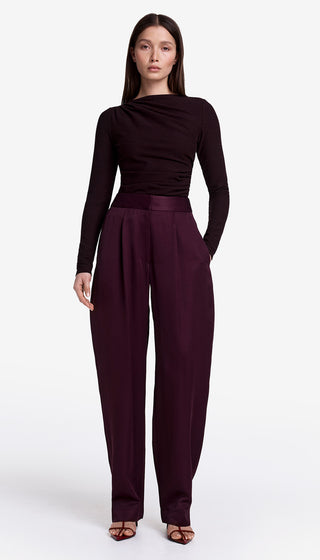 Woman wearing a black long-sleeve top and burgundy pants on a white background