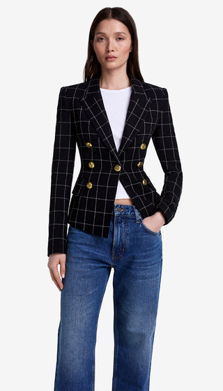 Woman wearing a black checkered blazer with gold buttons and blue jeans on a white background