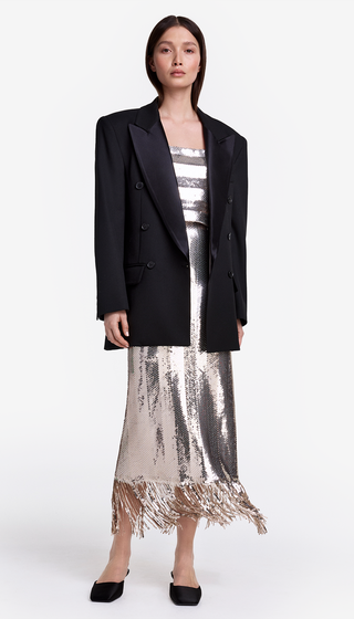 Woman wearing a black blazer, striped top, and sequin skirt on a white background