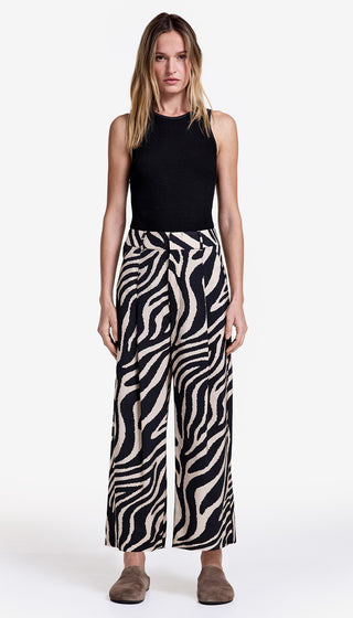 Woman wearing a black sleeveless top and zebra print pants on a white background