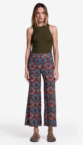 Woman wearing a green sleeveless top and patterned pants on a white background