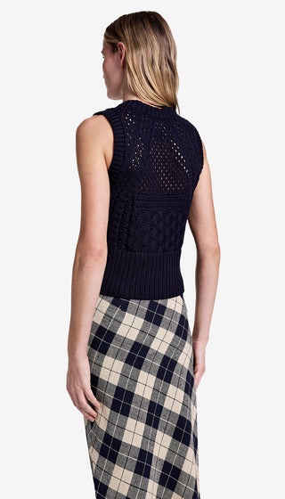 Woman wearing a navy sleeveless knitted top and plaid skirt on a white background