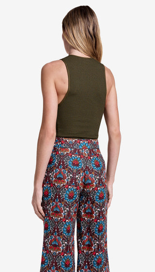 Person wearing a green sleeveless top and colorful patterned pants on a white background