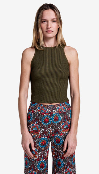 Woman wearing a green sleeveless top and patterned pants on a white background