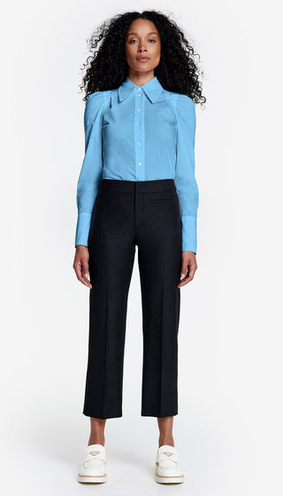 A person wearing a blue shirt and black cropped trousers with a front welt detail, standing against a white background.