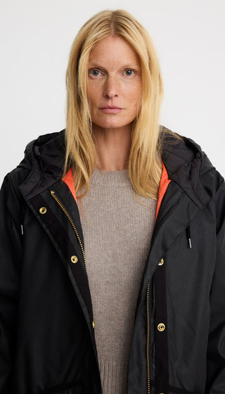 Person wearing a black jacket with a hood and orange lining on a white background