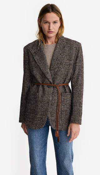 Woman wearing a patterned blazer with a belt and jeans on a white background