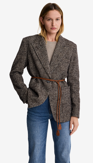 Woman wearing a checkered blazer with a belt and blue jeans on a white background
