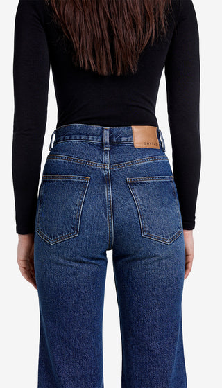 Person wearing blue jeans and a black long-sleeve top on a white background
