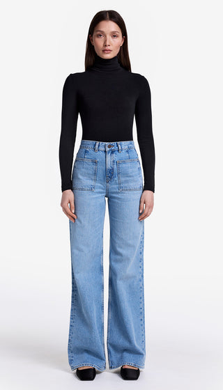 Person wearing a black turtleneck and light blue jeans on a white background