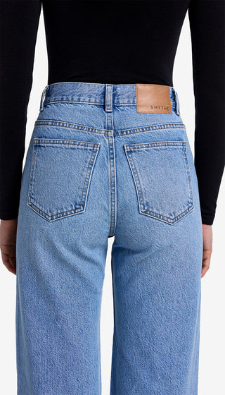 Person wearing blue jeans with a brand label on the back pocket against a white background