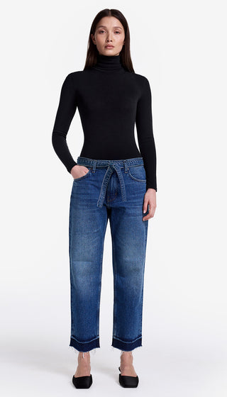 Woman wearing a black turtleneck and blue jeans on a white background