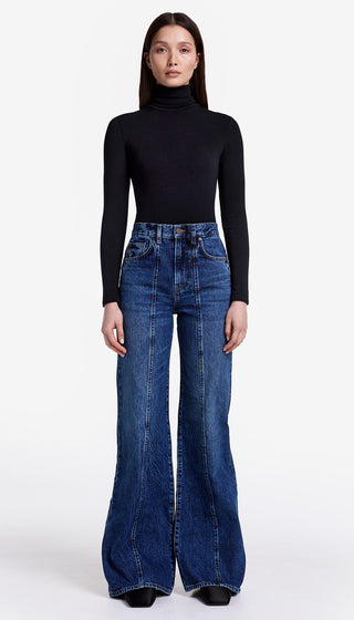 Person wearing a black turtleneck and blue flared jeans on a white background