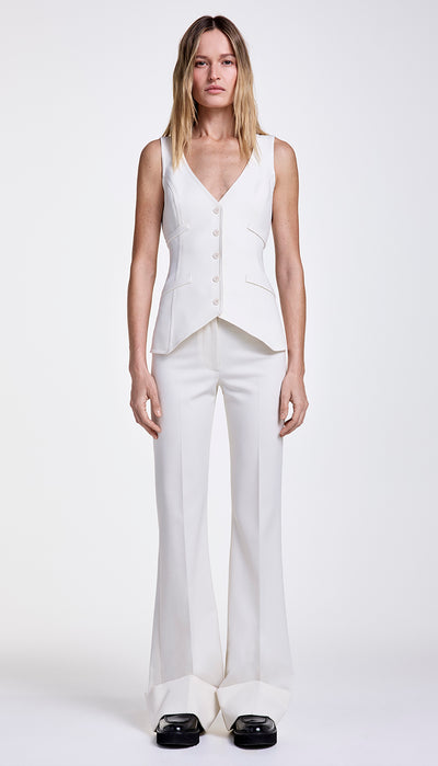 A model wearing a coordination of white sleeveless blazer, waistcoat, and wide leg cuffed trouser with a deep hem cuff.
