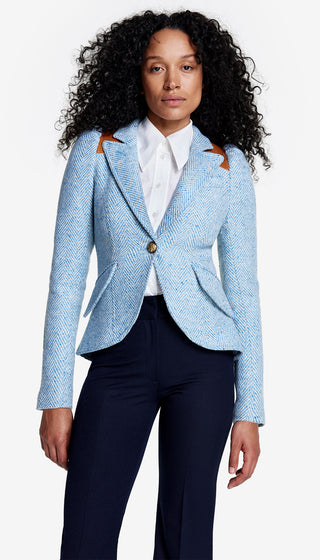 Woman wearing a light blue blazer with brown buttons and navy pants on a white background