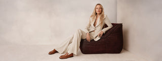Woman sitting on a brown bean bag chair against a plain background
