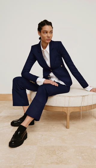 Person wearing a navy suit sitting on a white stool against a light background