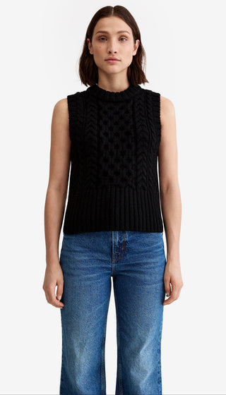 Woman wearing a black sleeveless knitted top and blue jeans on a white background