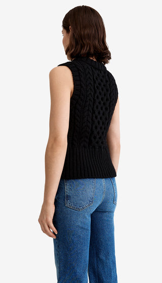 Person wearing a black sleeveless knitted top and blue jeans on a white background