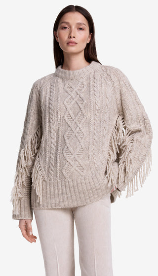 Woman wearing a beige cable knit sweater with fringe details on a white background