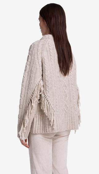 Woman wearing a textured beige cardigan with fringe details on a white background