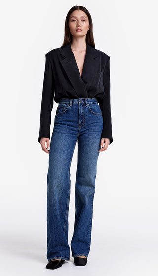 Woman wearing a black blazer and blue jeans on a white background