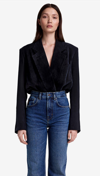 Woman wearing a black blazer and blue jeans on a white background