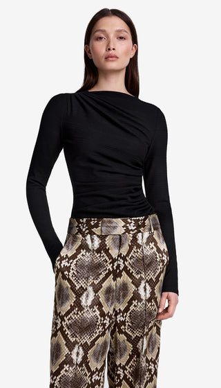 Woman wearing a black long-sleeve top and snake print pants on a white background
