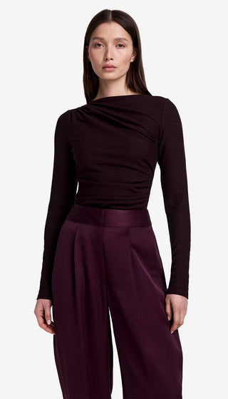 Woman wearing a dark long-sleeve top and purple pants on a light gray background