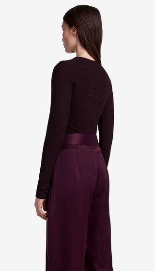 Person wearing a dark long-sleeve top and burgundy wide-leg pants on a white background