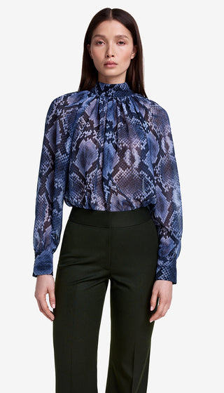 Woman wearing a blue snake print blouse and black pants on a white background