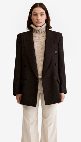 Woman wearing a dark brown blazer over a beige turtleneck sweater on a white background