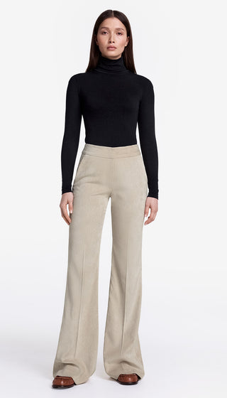 Woman wearing a black turtleneck and beige high-waisted pants on a white background