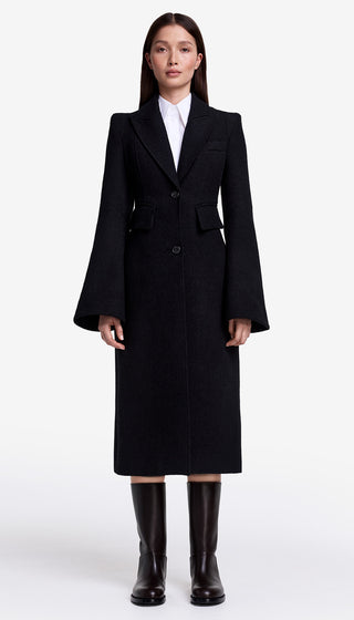 Person wearing a long black coat and black boots on a white background