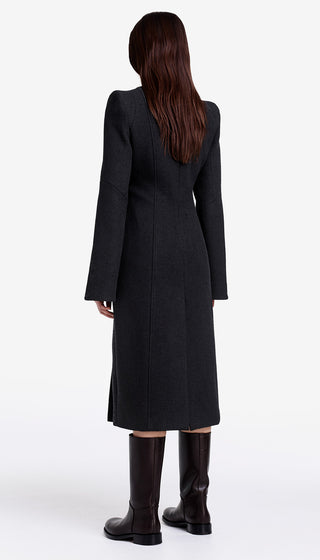 Person wearing a long black coat and boots on a white background