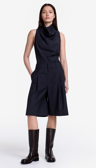 Woman wearing a black sleeveless dress with a cowl neck and knee-length skirt on a white background.