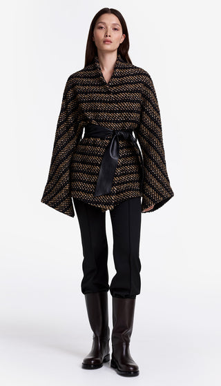 Woman wearing a patterned poncho, black pants, and boots on a white background